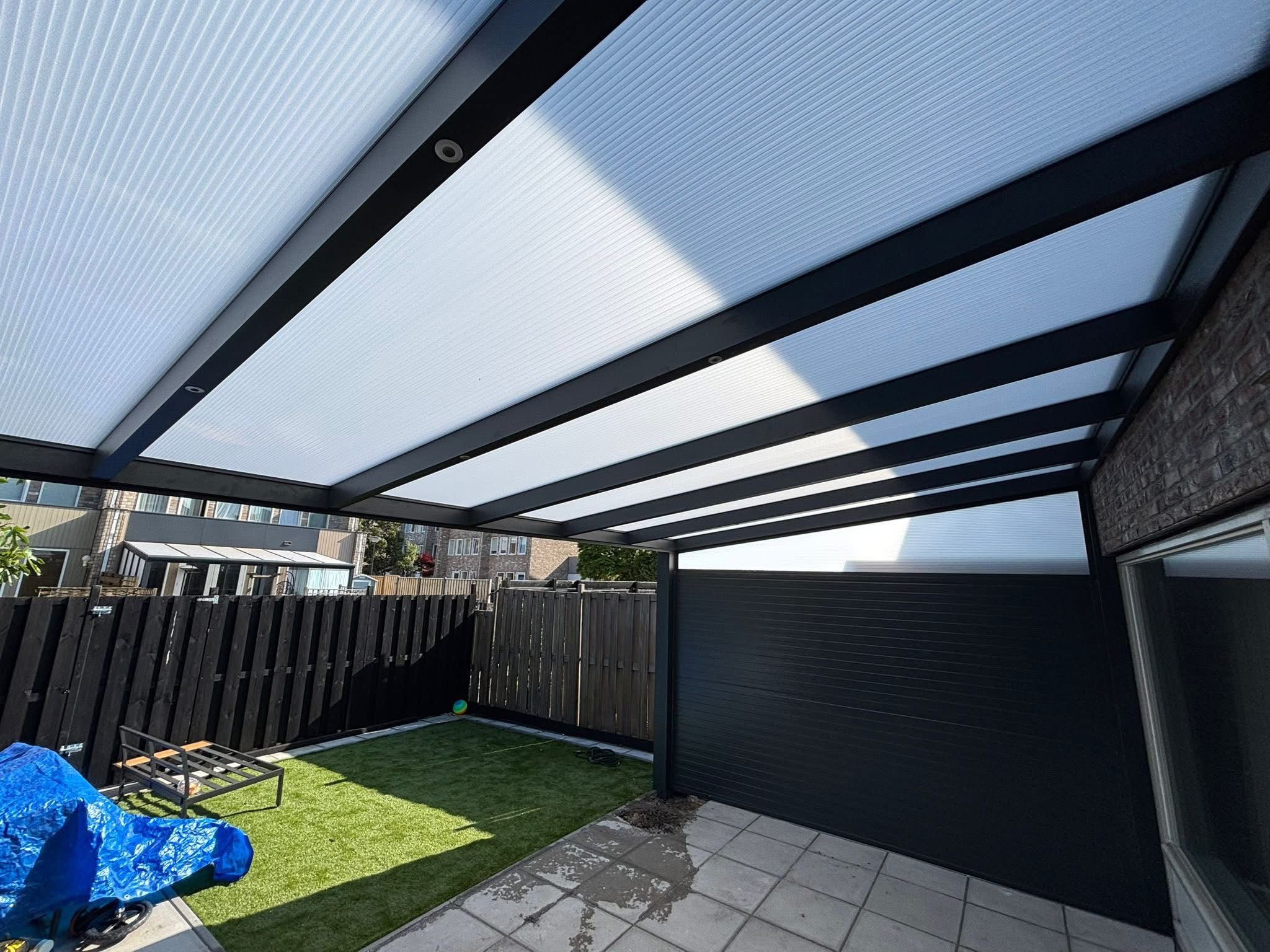 Blik van onder de veranda op het polycarbonaat dak, de aluminium liggers en de gesloten zijwand